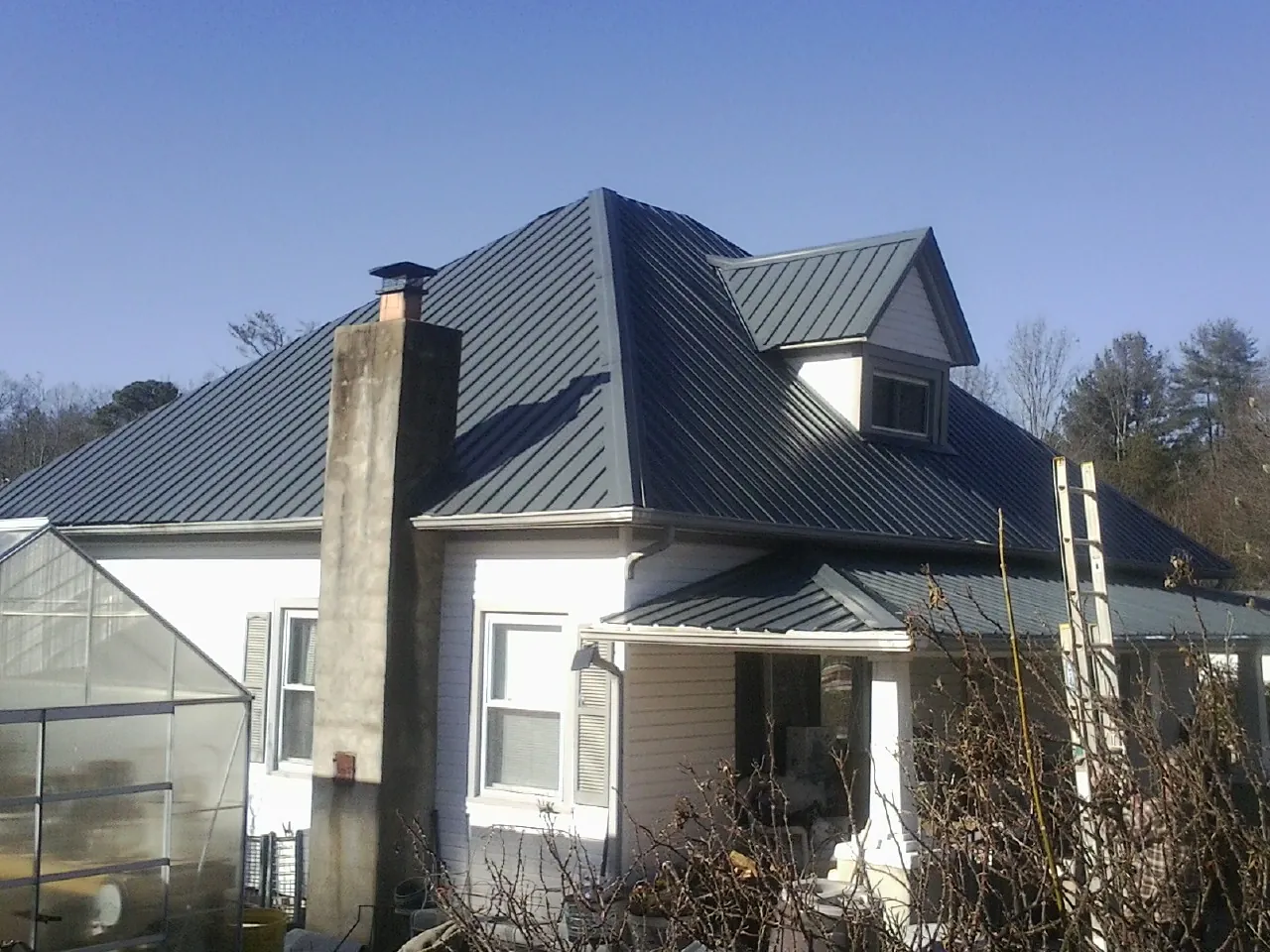 Dark blue standing seam metal roof on a white farmhouse with dormer — Slate & Tile Roof Repair by Roofing Brothers in Greenbelt