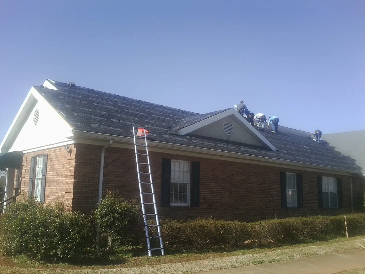 Crew tearing shingles off a brick ranch roof with a ladder set — Emergency Roof Repair work by our crew in Greenbelt