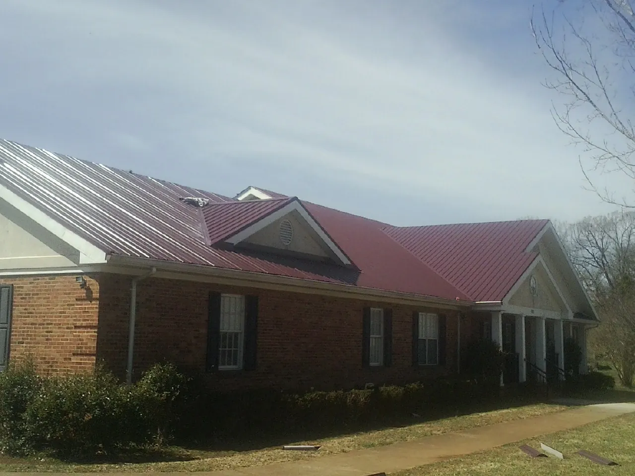 Red metal roof with gabled entries on a long brick building, from a Hail Damage Roof Repair job in Greenbelt