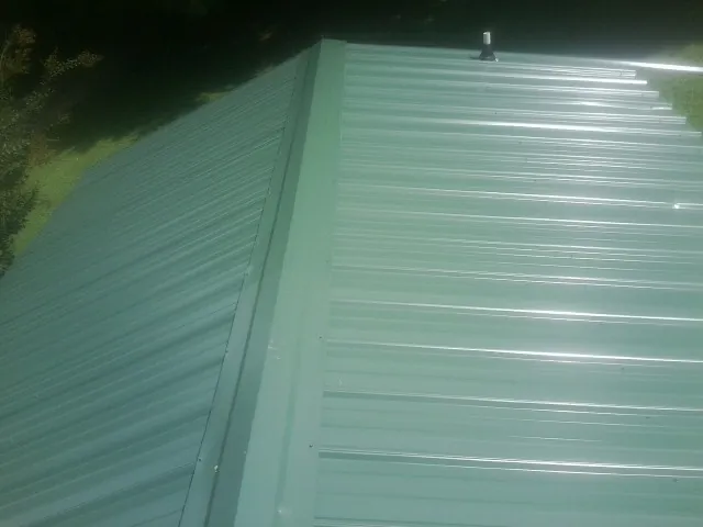 New green metal panels meeting at the ridge of a roof — Flat Roof Repair work by our crew in Greenbelt