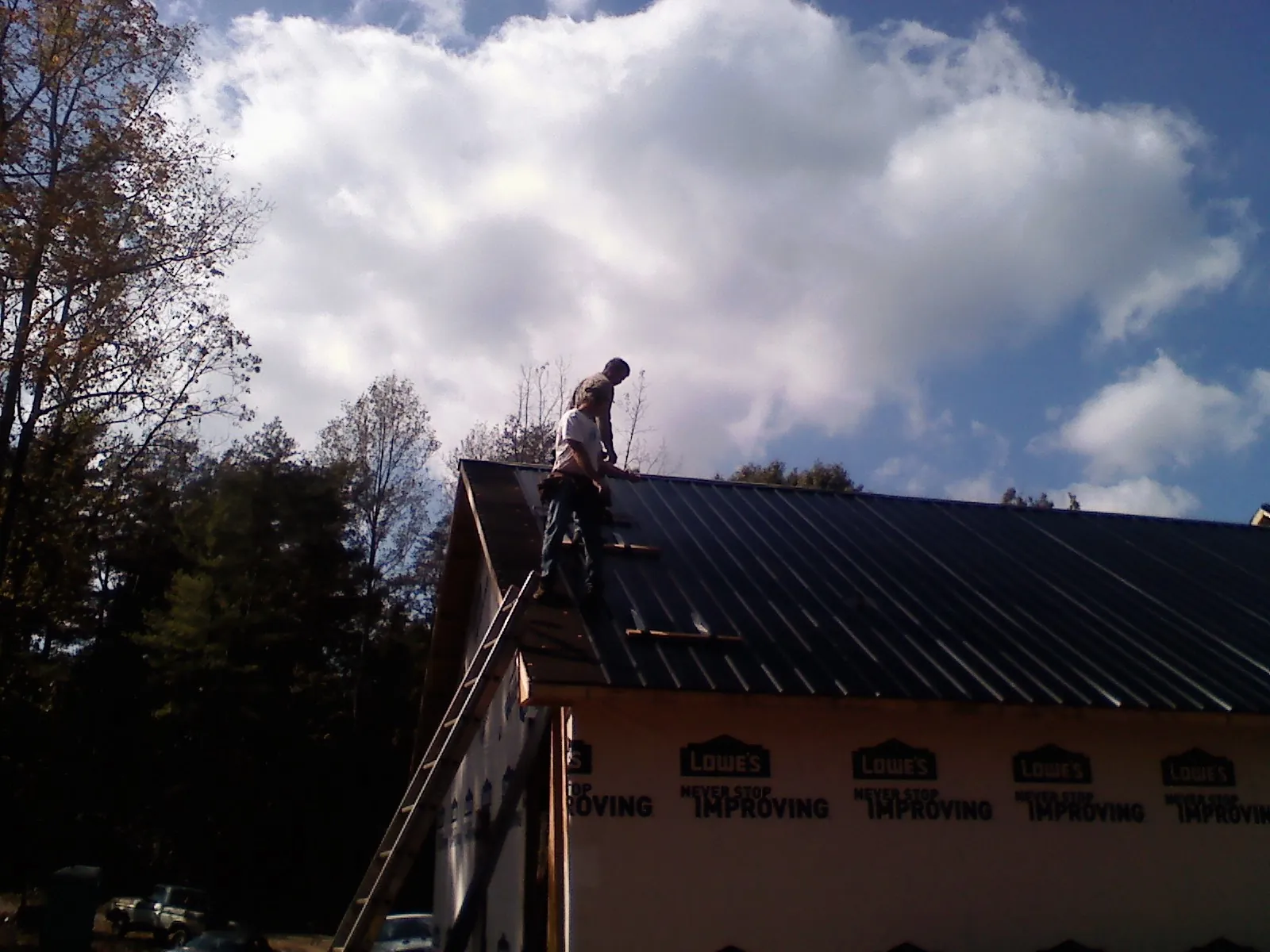 Roofer fastening dark metal panels high against a cloudy sky, from a Roof Inspection job in Greenbelt