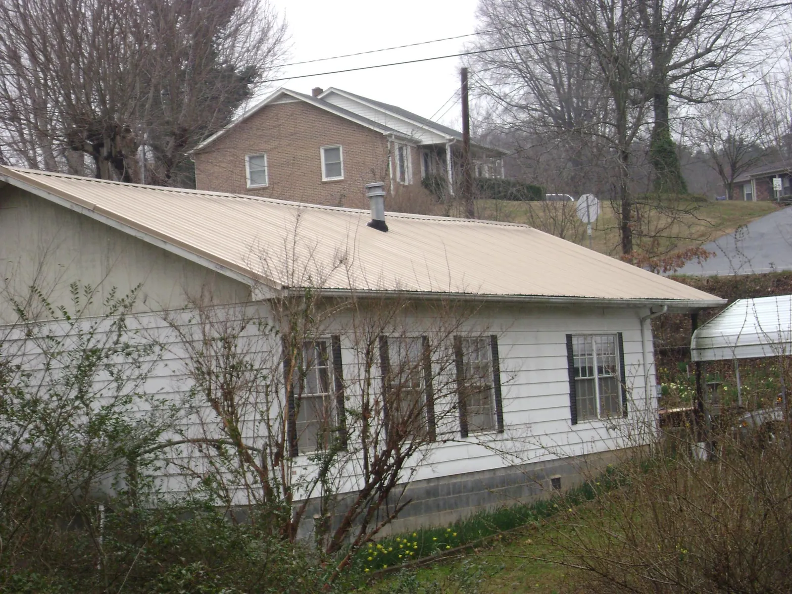 Tan metal roof on a white sided house set into a hillside — Commercial Roofing by Roofing Brothers in Greenbelt